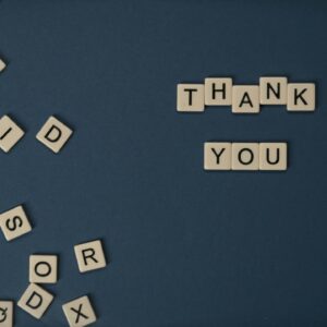 Top view of scattered Scrabble tiles with Thank You spelled out on blue surface.