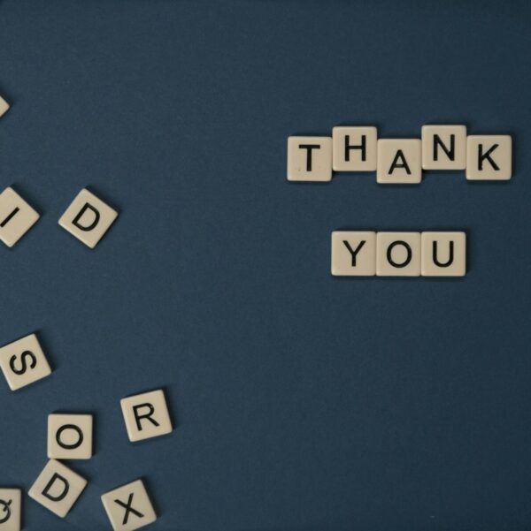 Top view of scattered Scrabble tiles with Thank You spelled out on blue surface.